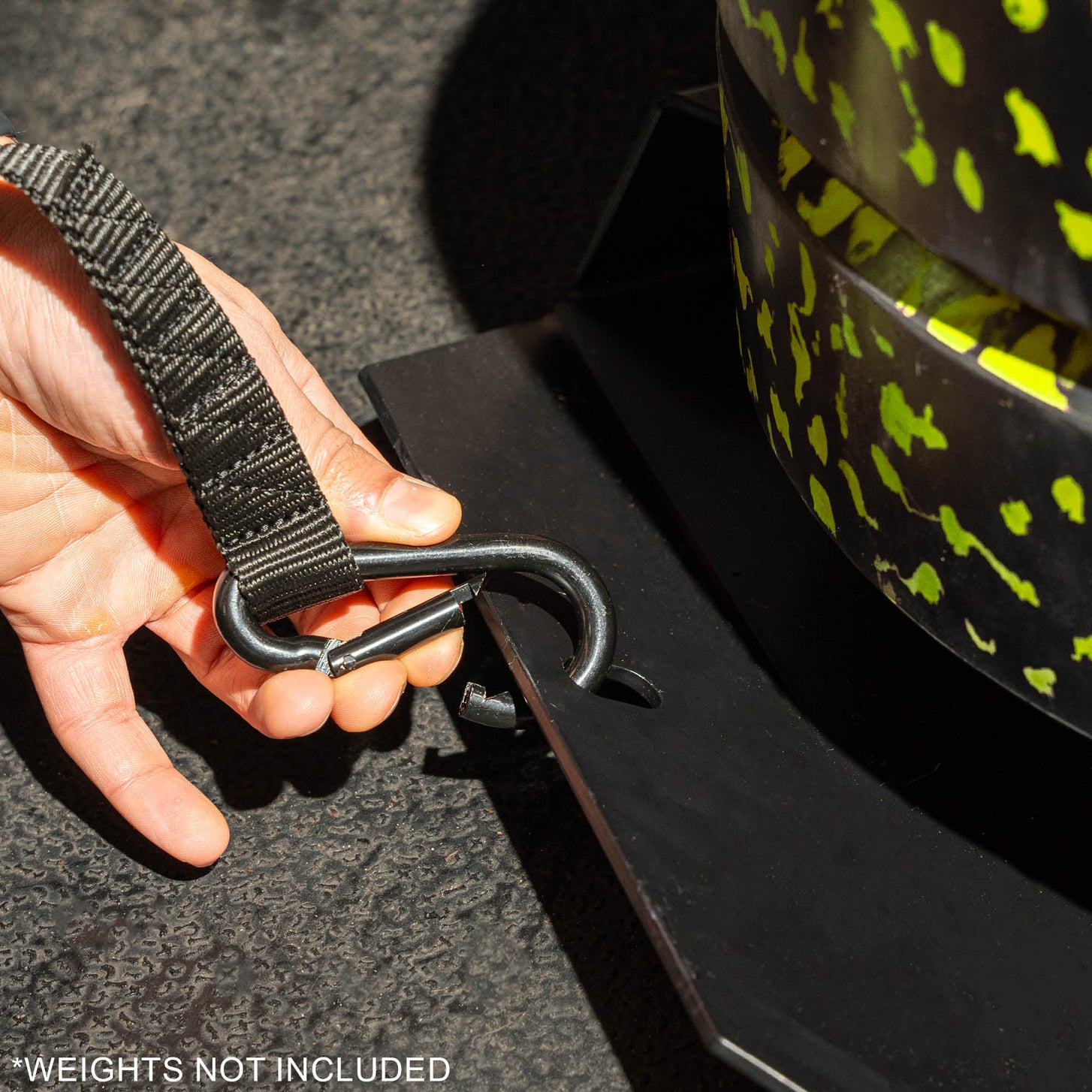 Hand clipping a strap's metal snap hook onto the edge of the Pull Speed Sled, with the text "Weights not included".