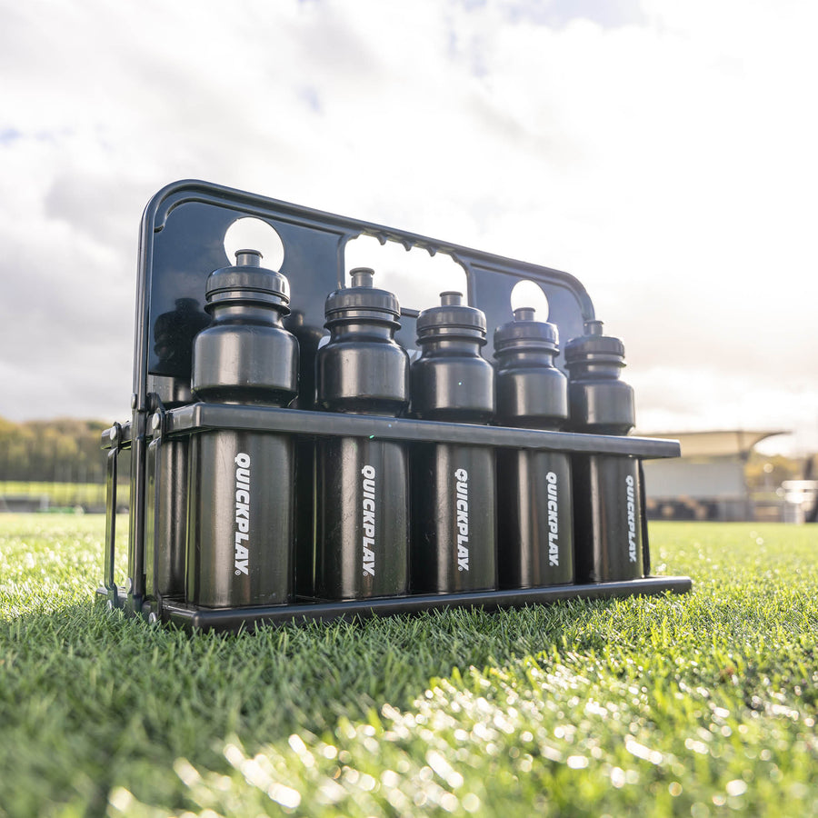 Black water bottle holder with six bottles labeled 'Quickplay' on grass