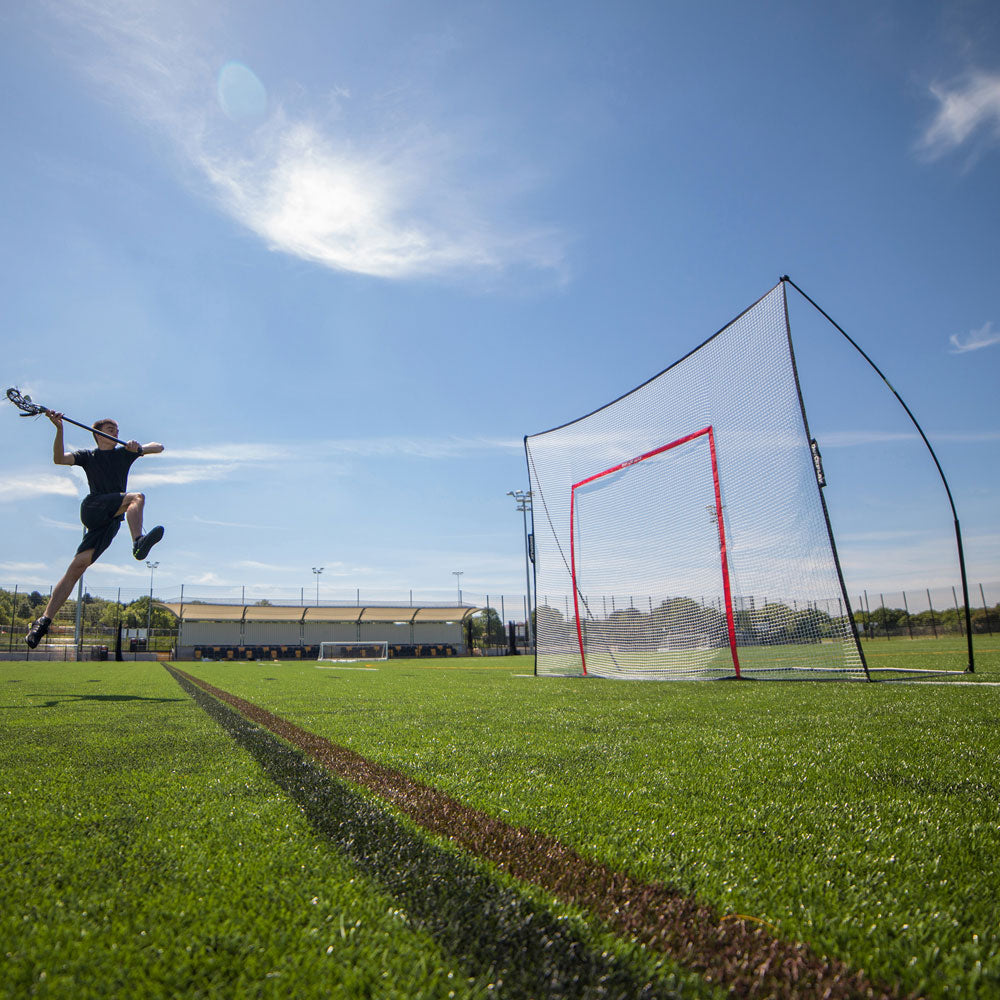 Lacrosse player jumping to shoot at a MEGA NET with a target frame on an artificial pitch.