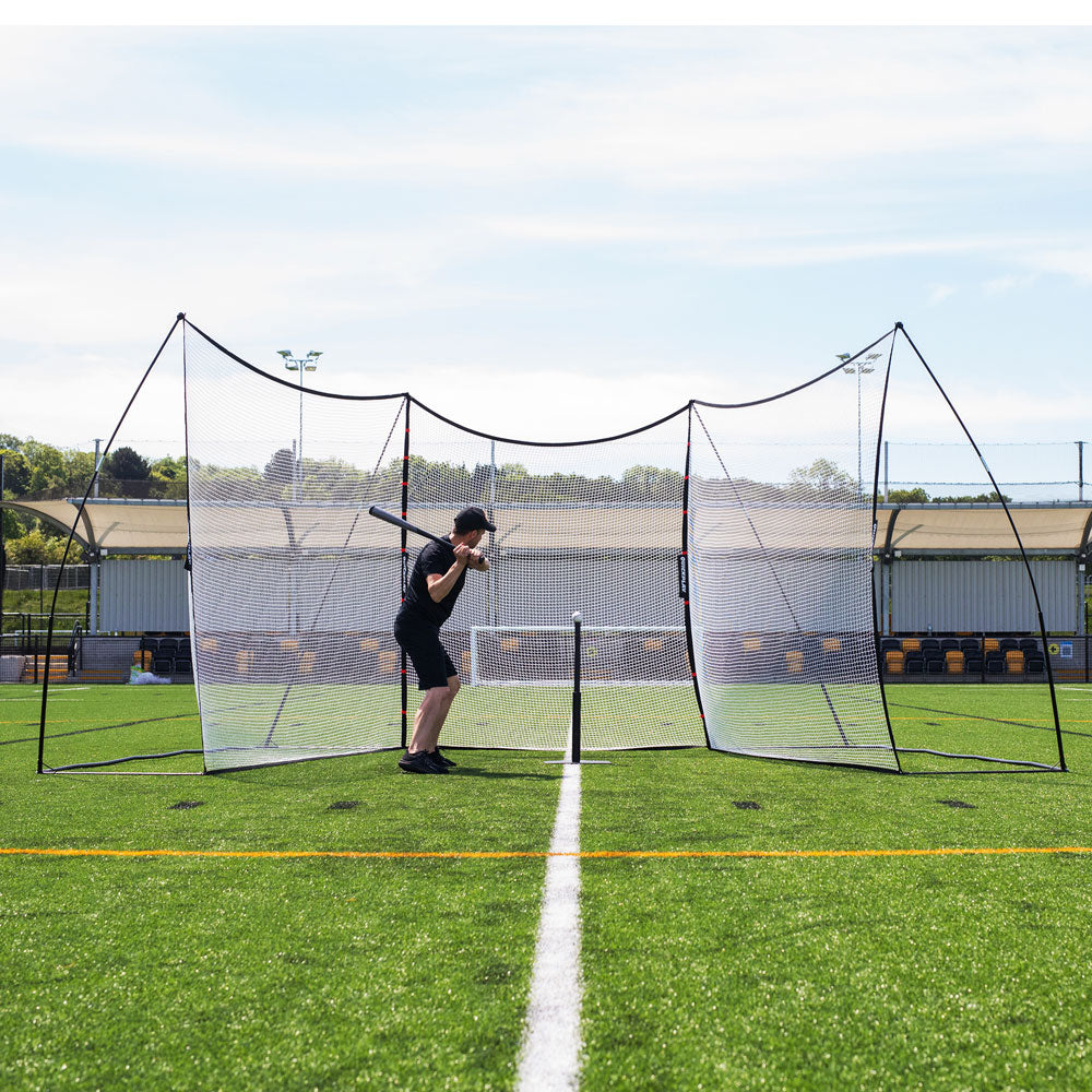 Man batting in front of the MEGA NET XL Ball-Stop 32x9', seen from the front on an artificial pitch.