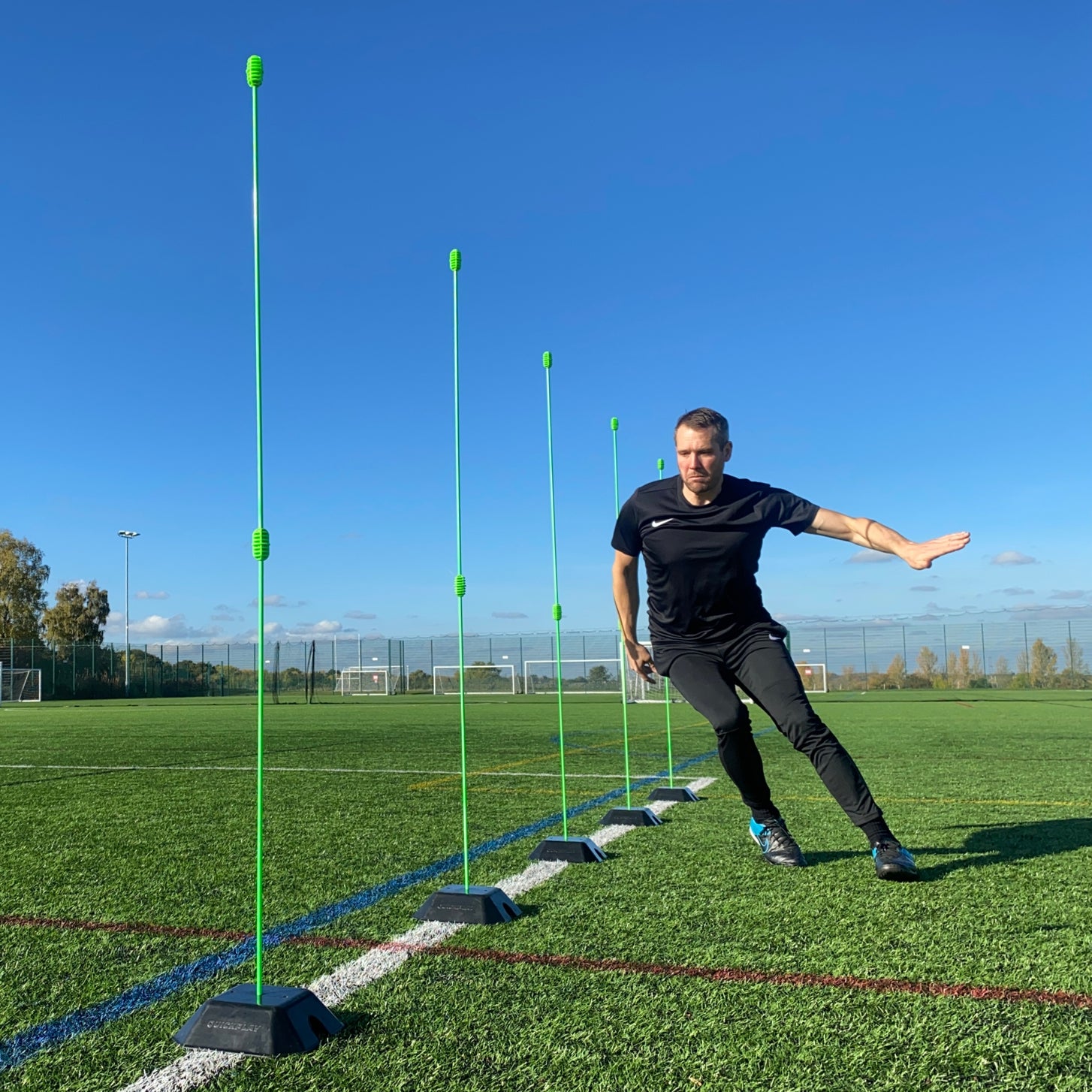 Man side-stepping beside a line of green poles set in black QUICKPLAY base weights on an artificial pitch.