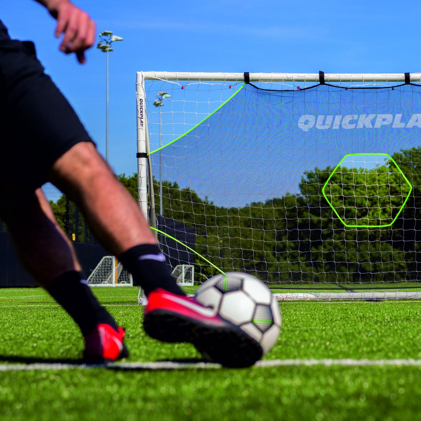 Player about to strike a ball at the TARGET Net Lite 6x4' and its green hexagon target on an artificial pitch.