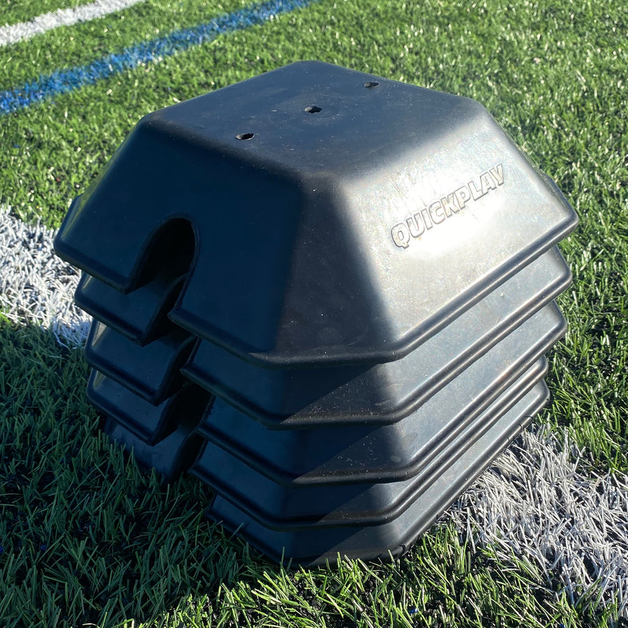 Stack of black QUICKPLAY base weights on artificial grass, showing how they nest together.